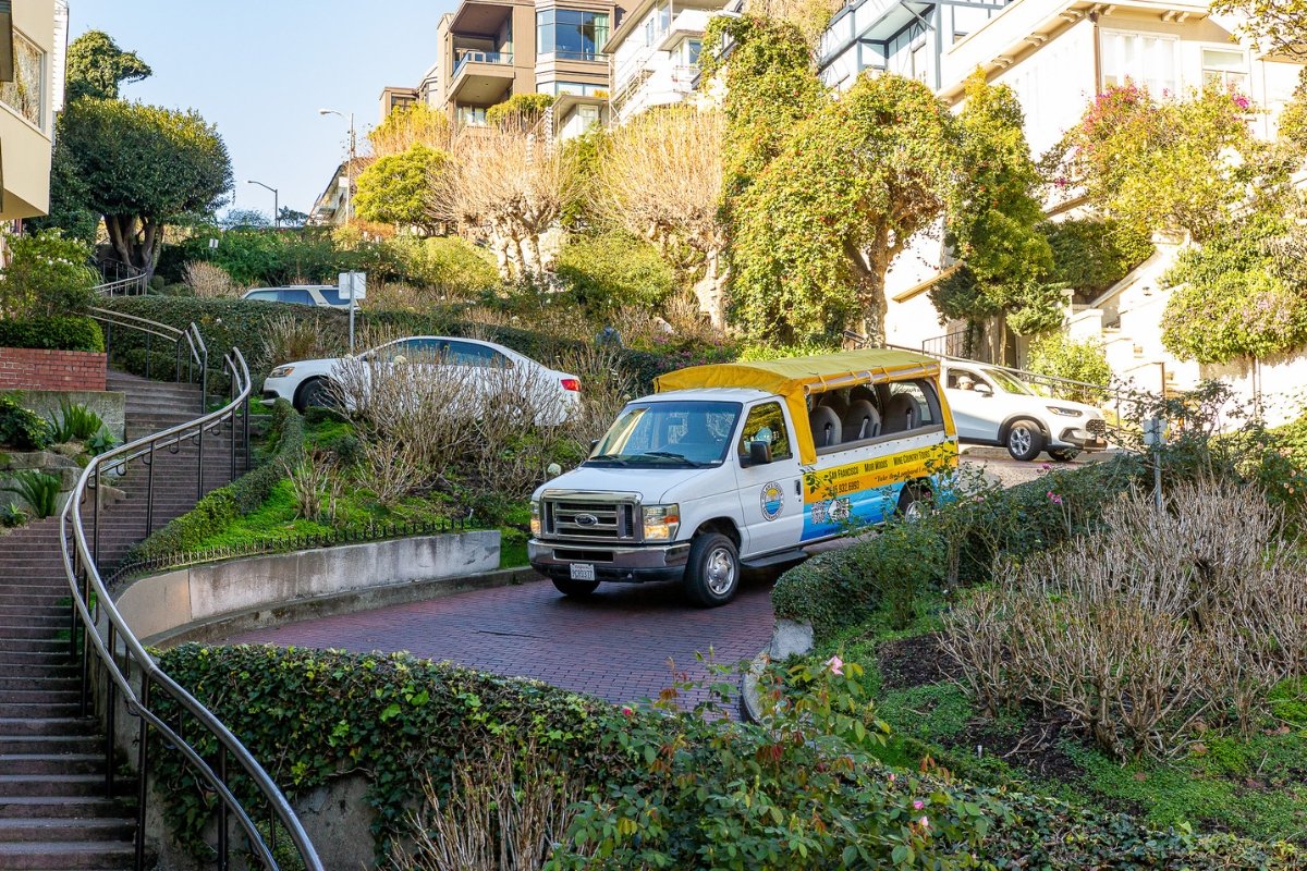 Dylan's Tours sightseeing van driving on a brick-paved curved road surrounded by lush landscaping and terraced apartment buildings in San Francisco.