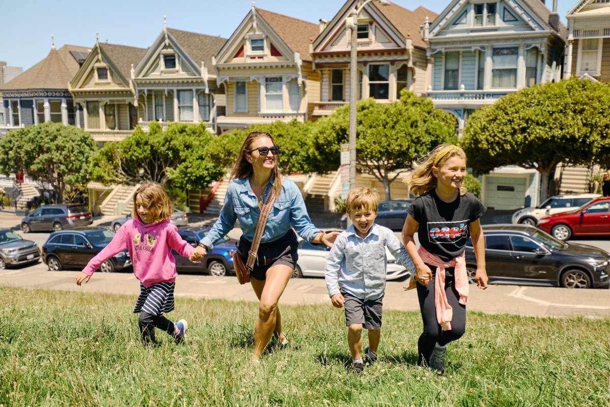 Colorful row of Victorian Painted Ladies houses in San Francisco with family holding hands running in grassy foreground