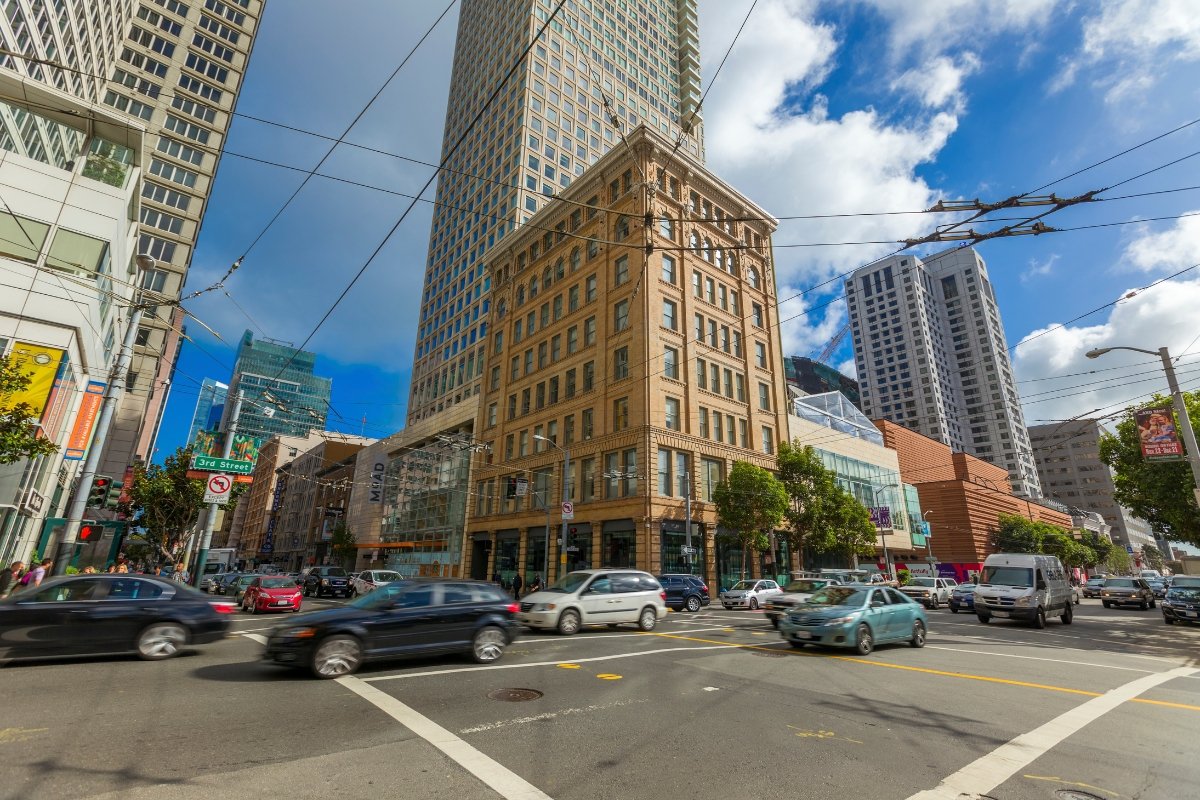Historic terra cotta building at busy San Francisco intersection with modern skyscrapers and overhead cable car lines
