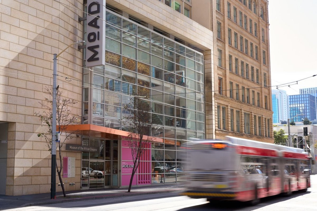 Modern glass facade of Museum of the African Diaspora in San Francisco with city bus passing by and downtown buildings