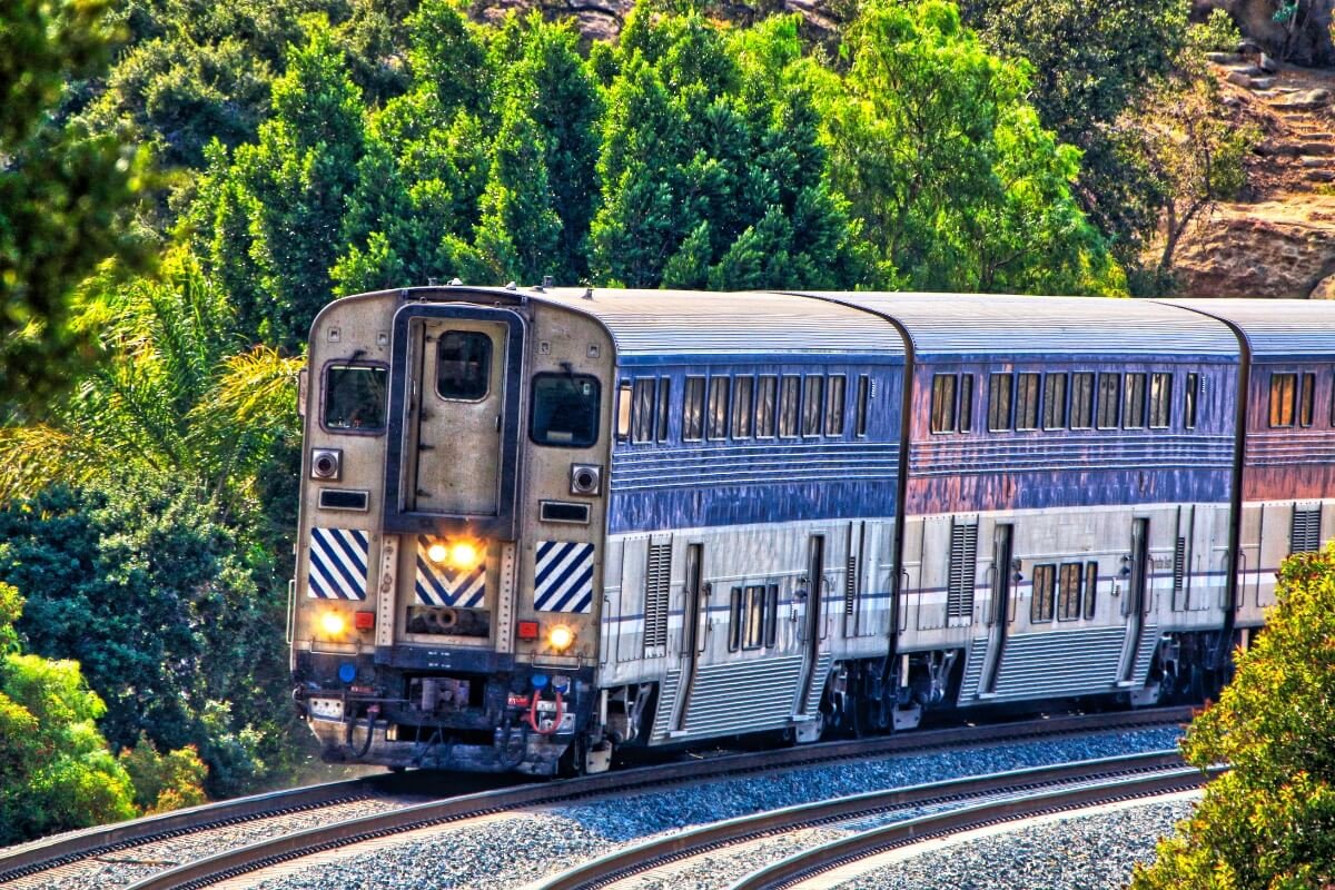 Silver and blue Caltrain passenger train traveling through lush green California hillside