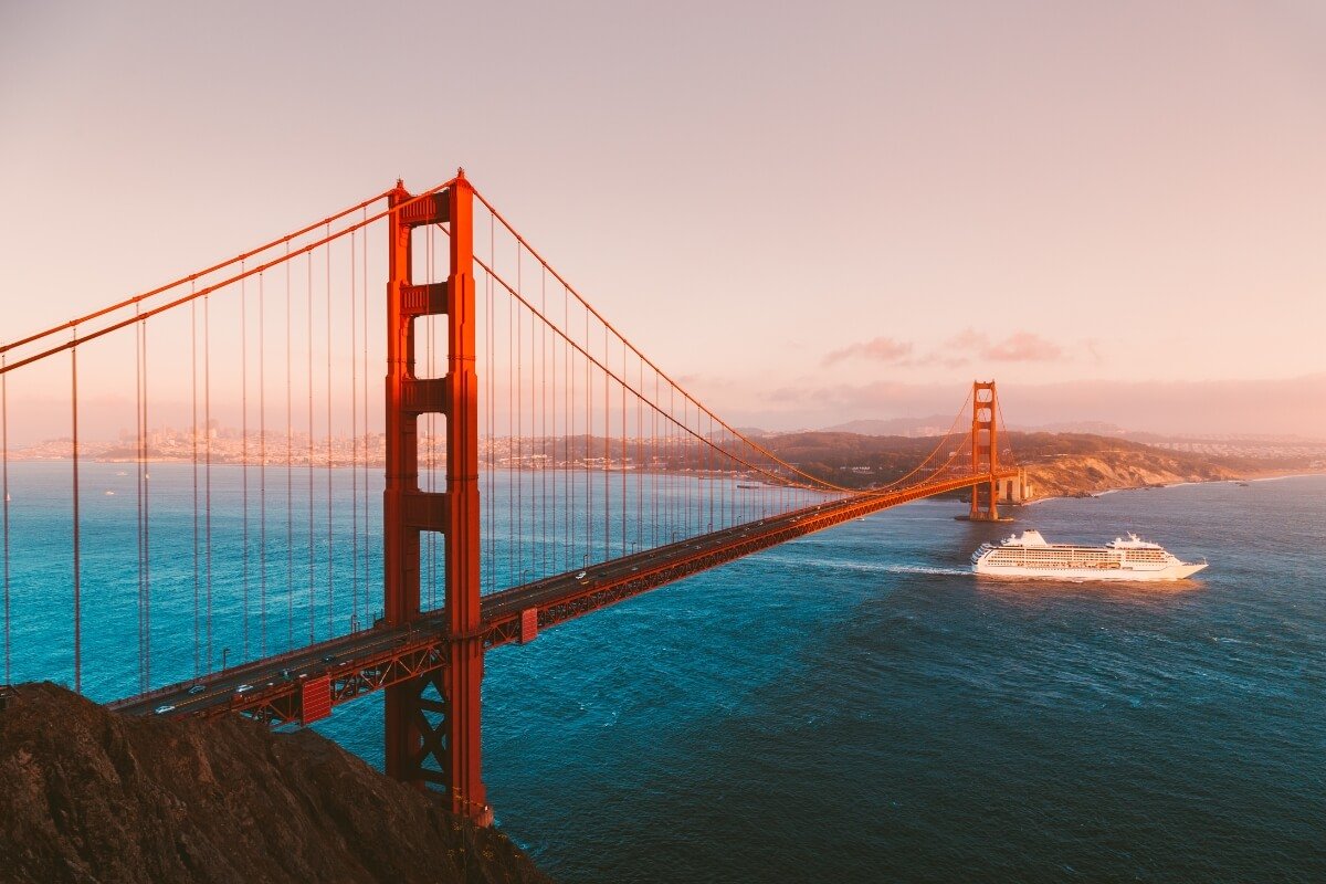 Iconic orange Golden Gate Bridge at sunset with cruise ship passing beneath and San Francisco Bay waters