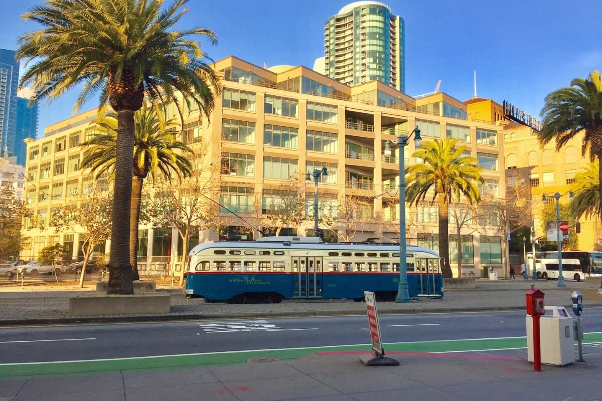 Vintage blue and white F-Market streetcar on Embarcadero with palm trees and waterfront buildings