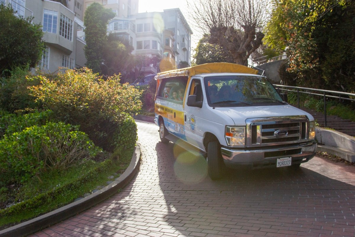 Open-air tour van from Dylan's Tours climbing a steep San Francisco hill with sunlight illuminating the city's residential buildings in background