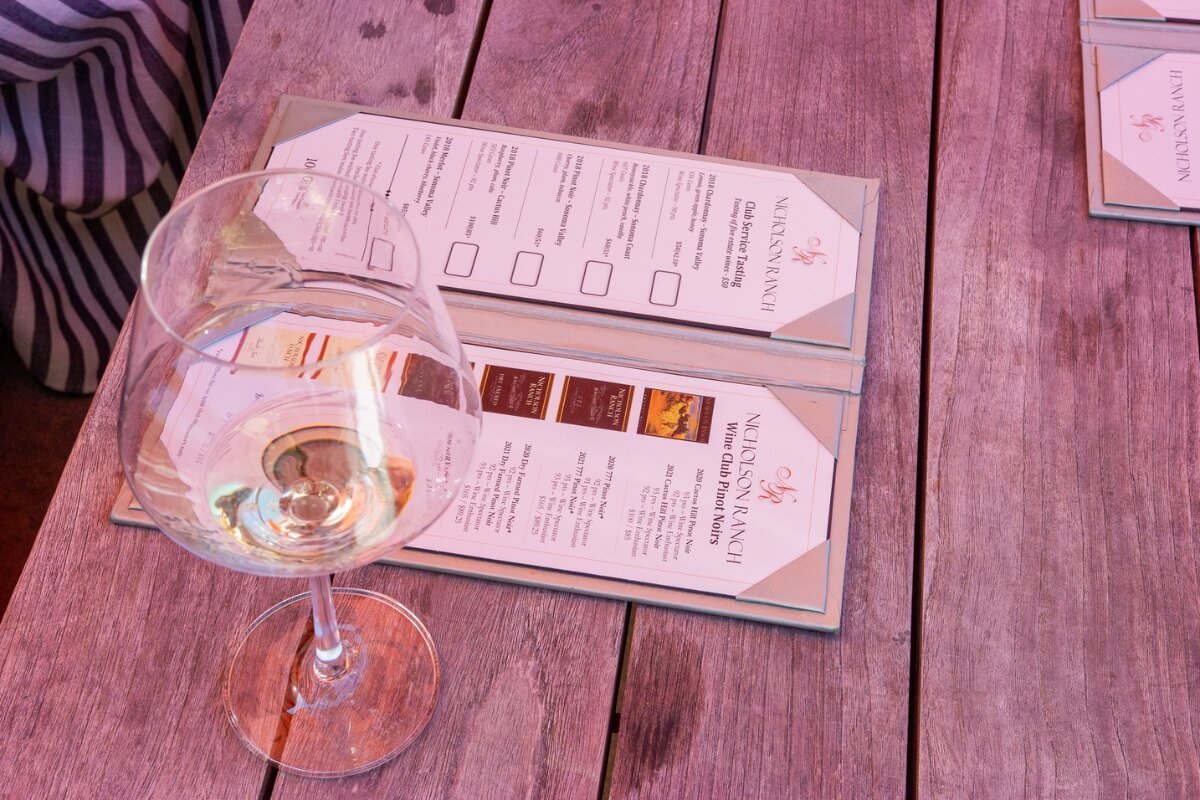 Wine tasting menu at Nelson Ranch vineyard with glass of white wine on rustic wooden table in California wine country.