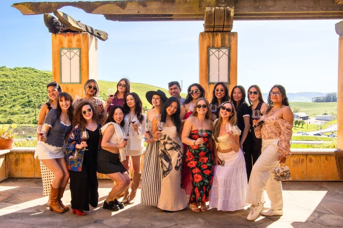 Group of wine tour participants posing with glasses at scenic California winery with rolling vineyard hills