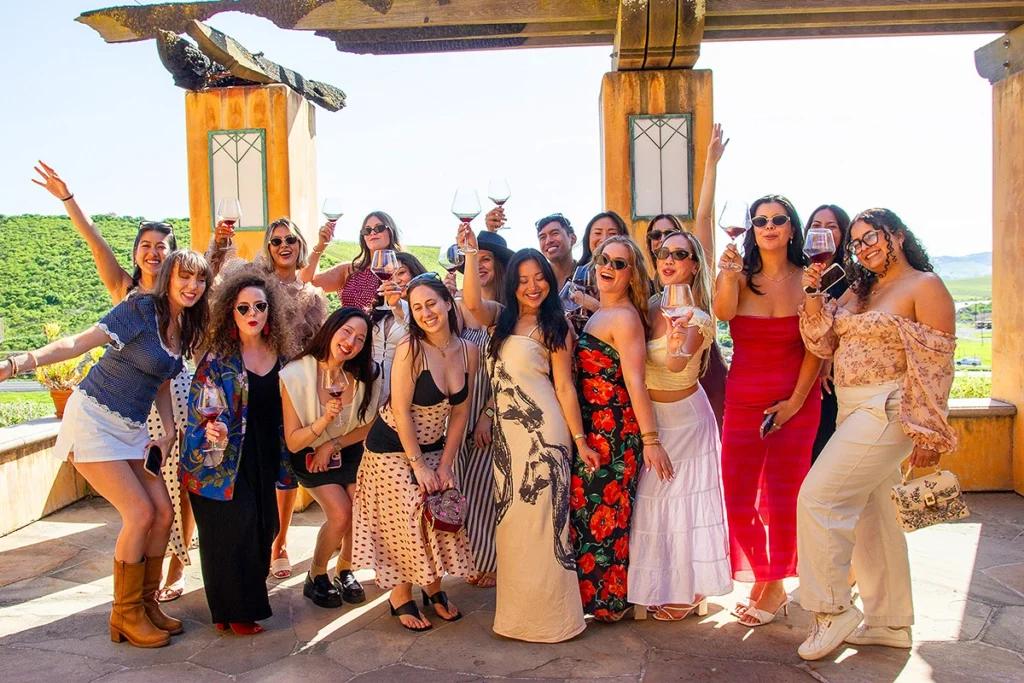 Group of women enjoying wine outdoors with vineyard views, smiling and relaxed, capturing the social and scenic experience of wine country.