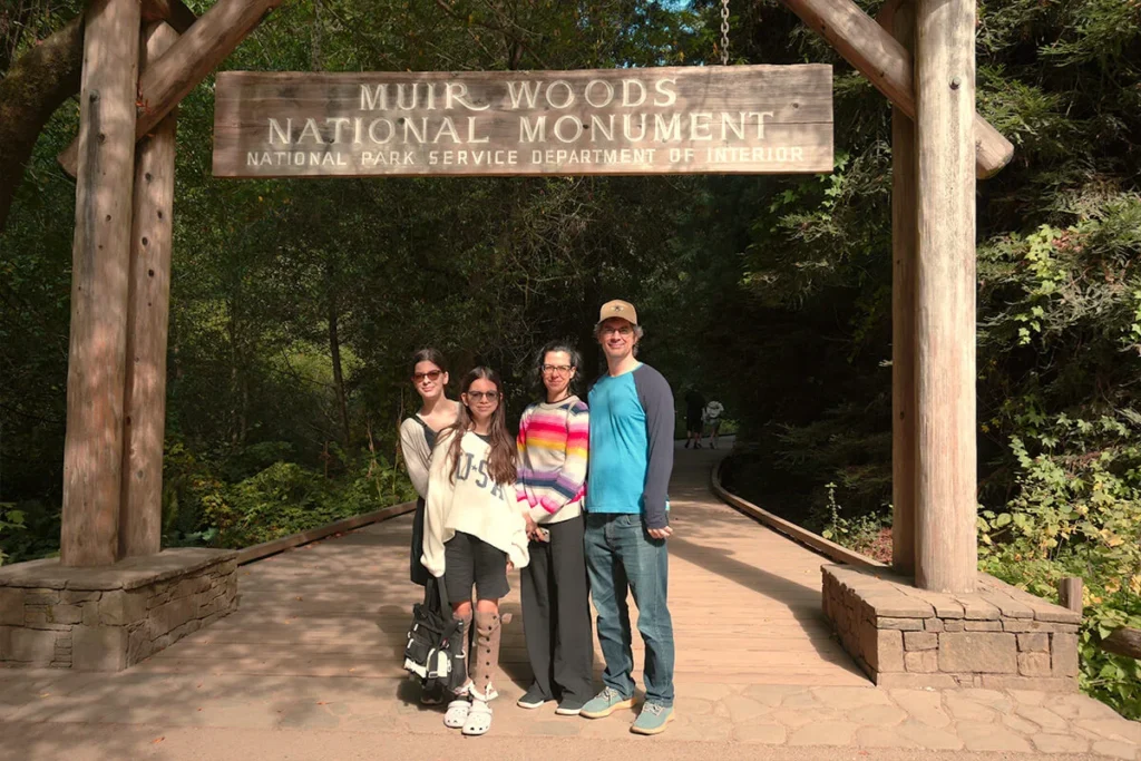 Family posing for a photo at the entrance sign of Muir Woods National Monument
