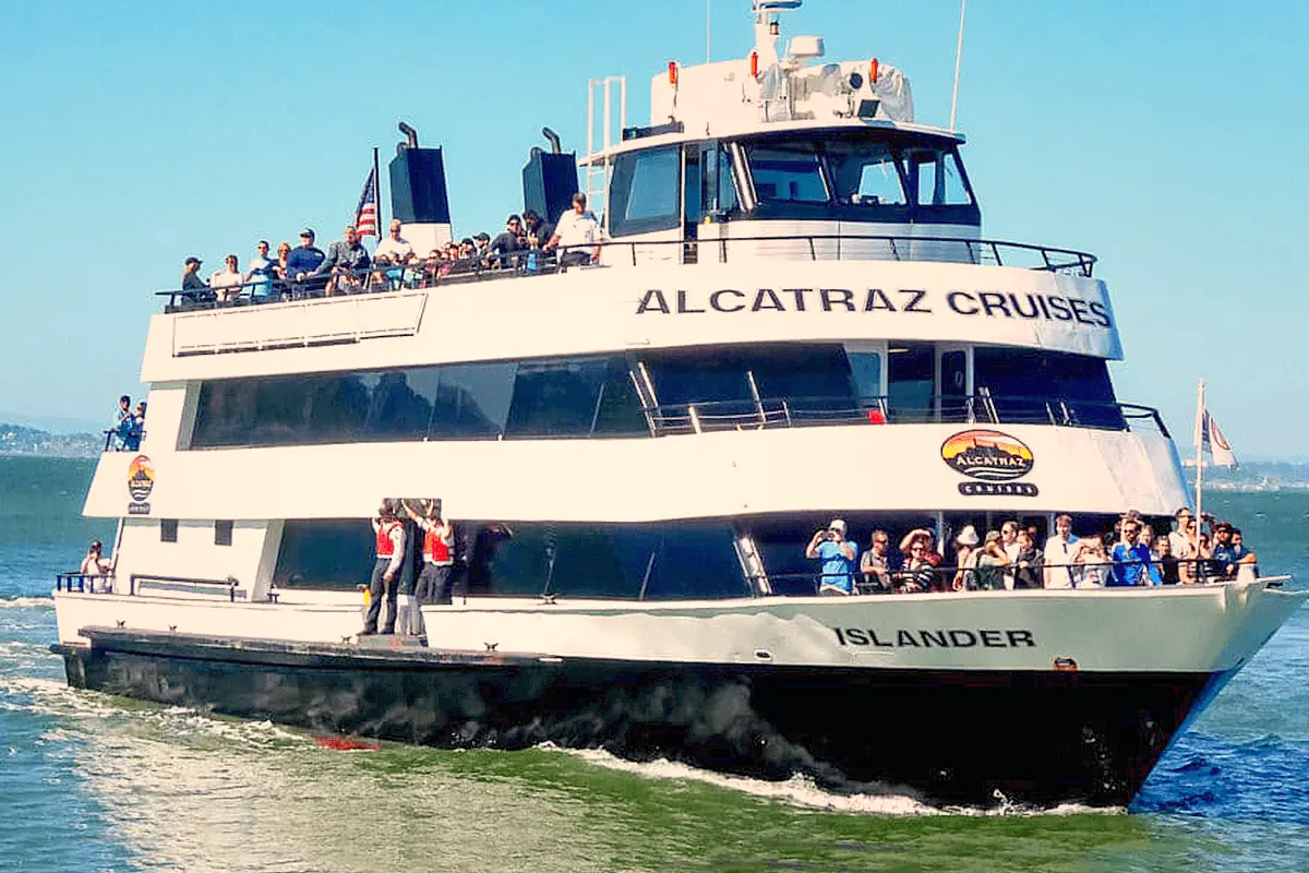 Tourists aboard a cruise ship approaching Alcatraz Island, with the historic prison visible in the background