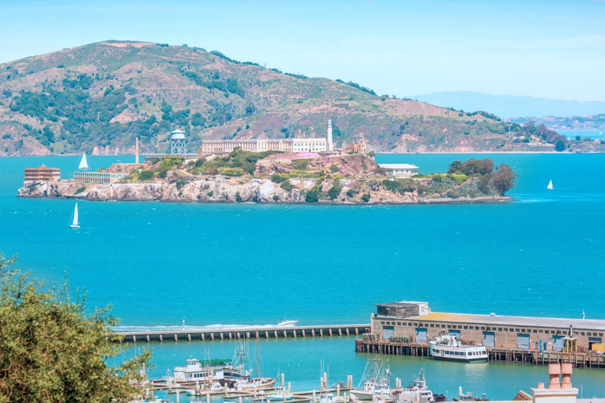 Scenic view of Alcatraz Island from San Francisco Pier with sailboats on the bay.