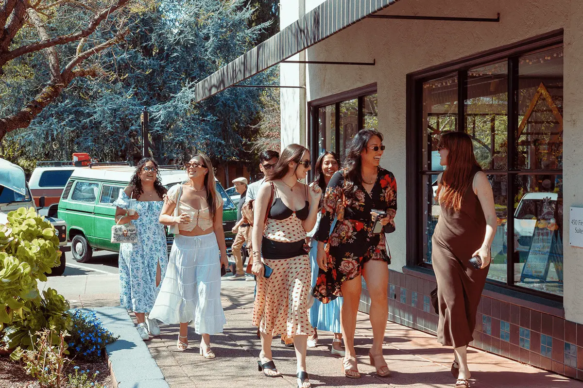 Group of friends walking together along a vineyard path, surrounded by grapevines and greenery on a sunny day.