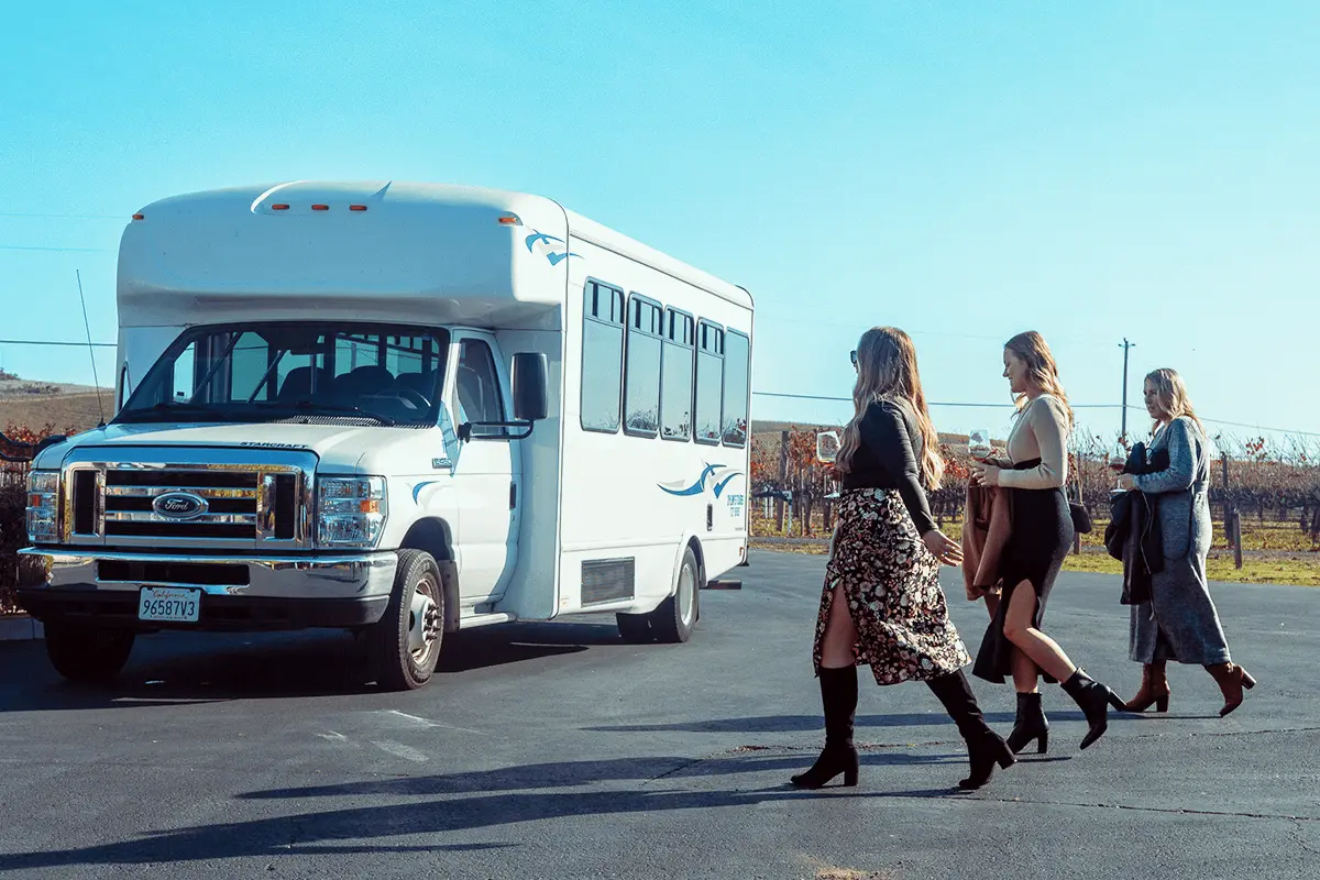 Guests walking toward a vineyard entrance, passing under an archway with grapevines and autumn foliage in the background.
